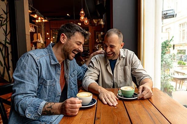 Twee lachende vrienden praten bij koffie aan een houten cafétafel